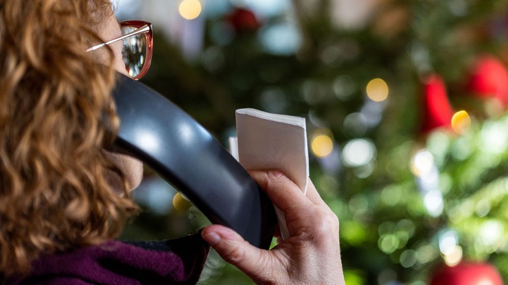 (Symbolbild) Eine Frau sitzt mit dem Telefon vor einem Weihnachtsbaum. | Bild: dpa-Bildfunk/Jens Büttner