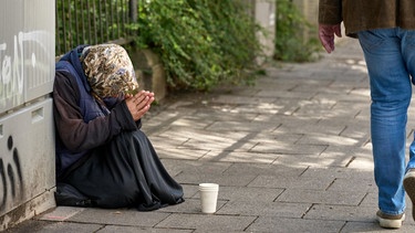 Ältere Dame beim Betteln am Straßenrand in München, betet für Unterstützung. Ein Passant läuft an ihr vorbei. Symbolbild Altersarmut | Bild: picture alliance / CHROMORANGE | Michael Bihlmayer