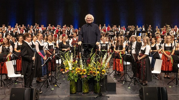 Auf dem Dirigentenpult steht Sir Simon Rattle - vor 300 Musikern aus vier Blaskapellen und dem Bayerischen Symphonieorchester. | Bild: BR/ Markus Konvalin