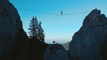 Ein Mann balanciert über eine zwischen zwei Berggipfeln gespannte Highline.  | Bild: The Gap/Jascha Polenz