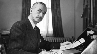 Der Schriftsteller Thomas Mann im Exil in den USA im Jahr 1943, an seinem Schreibtisch sitzend, in einer Hand seine Brille, in der anderen ein Schriftstück | Bild: picture alliance/ Fred Stein