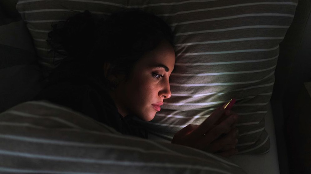 Eine Frau scrollt durch ihr Handy, liegt im Dunklen in ihrem Bett. | Bild: picture alliance / Image Source | Eugenio Marongiu