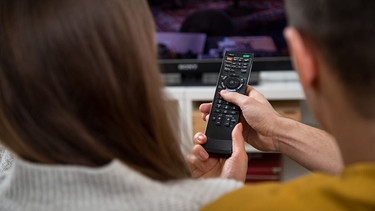 Mann und Frau auf einem Sofa bedienen einen Smart-TV per Fernbedienung. | Bild: picture alliance / dpa Themendienst | Christin Klose