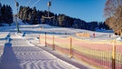 Eine sonnige Piste, die schneebedeckten Nadelbäume werfen lange Schatten, am Schlepplift hängen Eiszapfen. | Bild: BR/Markus Wessely