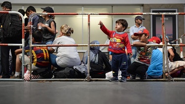 Flüchtlinge aus Syrien, die auf ihre Registrierung warten, stehen und sitzen am 31.08.2015 hinter einem Absperrgitter im Hauptbahnhof in München. | Bild: pa/dpa/Andreas Gebert