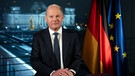 Der deutsche Bundeskanzler, Olaf Scholz, steht neben zwei Flaggen, einer von Deutschland und eine der europäischen Union. | Bild: picture alliance / Photoshot | -