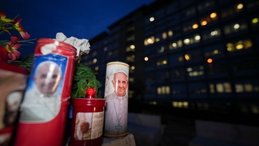 Kerzen mit Bildern von Papst Franziskus wurden unter der Statue des verstorbenen Papstes Johannes Paul II. vor der Poliklinik Agostino Gemelli in Rom niedergelegt, wo der Franziskus behandelt wird. | Bild: dpa-Bildfunk/Andrew Medichini