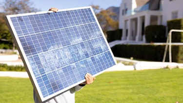 Eine Person hält ein kleines Solarpaneel in die Sonne, im Hintergrund ist Frühling. | Bild: dpa/pa/Zoonar/Channel Partners