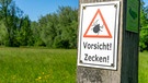 Schild mit der Aufschrift "Vorsicht! Zecken!" auf einer grünen Wiese (Symbol- und Archivbild) | Bild: picture alliance / Jochen Tack | Jochen Tack