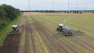 Vogelperspektive auf einen Acker im Emsland, auf dem die Wasserstoff-Protoyp-Traktoren von Fendt fahren. Beide haben einen weißen Kasten auf dem Dach, den Wasserstofftank. Im Hintergrund sind viele Windräder zu sehen. | Bild: BR