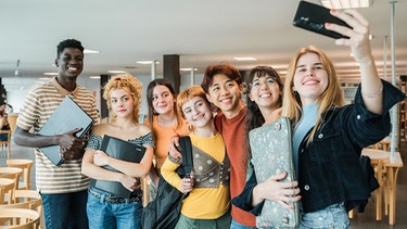 Eine Gruppe Jugendlicher steht nebeneinander, lächelt, ein Mädchen macht ein Selfie von der Gruppe. | Bild: colourbox.com