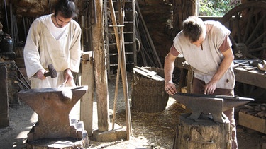 ARCHIV: Zwei Schmiede arbeiten am 21.09.2009 in einem Wald bei Guedelon (im französischen Burgund) auf einer mittelalterlichen Burg-Baustelle. | Bild: picture-alliance/dpa/Ulrike Koltermann