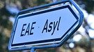 ARCHIV - 06.09.2023, Brandenburg, Eisenhüttenstadt: Ein Wegweiser mit der Abkürzung «EAE» und «Asyl» zur Erstaufnahme-Einrichtungen (EAE) des Landes Brandenburg in Eisenhüttenstadt. (Illustration zu dpa: "Gemeindebund zweifelt an schnellerem Asylverfahren und Bezahlkarte") Foto: Patrick Pleul/dpa +++ dpa-Bildfunk +++ | Bild: dpa-Bildfunk/Patrick Pleul