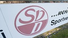 Das Logo von dem Fußballverein SV Donaustauf steht an einer Bande auf dem Gelände des Vereins in Donaustauf im Landkreis Regensburg. | Bild: pa/dpa