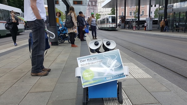 Roboter "Swa*lly" patroulliert mit seinem Schild "Der Kö ist Nichtraucher" ferngesteuert auf dem Augsburger Königsplatz. | Bild: BR/Torsten Thierbach