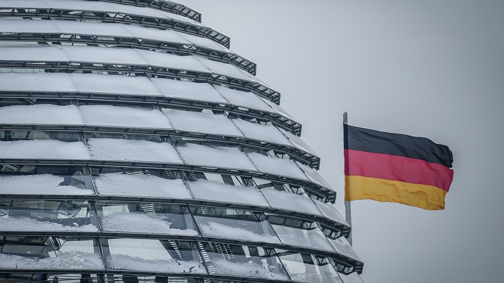 05.12.2023, Berlin: Die Deutschlandfahne weht neben der schneebedeckten Reichstagskuppel im Wind. Am Vormittag findet eine öffentliche Anhörung des Haushaltsausschusses zum Nachtragshaushalt 2023 und zur Aussetzung der Schuldenbremse als digitale Konferenz statt. Foto: Kay Nietfeld/dpa +++ dpa-Bildfunk +++ | Bild: dpa-Bildfunk/Kay Nietfeld