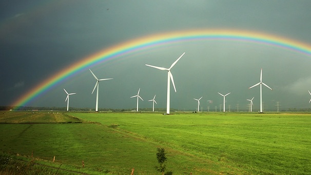 Ein Regenbogen spannt sich über grünen Feldern und Windkraftanlagen vor grauen Regenwolken | Bild: picture-alliance/dpa/Christian Charisius