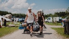 Festivalbesucher:innen sind mit viel Gepäck auf dem Weg zum Campingplatz des PULS Open Airs 2024. Impressionen vom Campingplatz während des PULS Open Air 2024 auf Schloss Kaltenberg. | Bild: BR/Julia Knoblauch