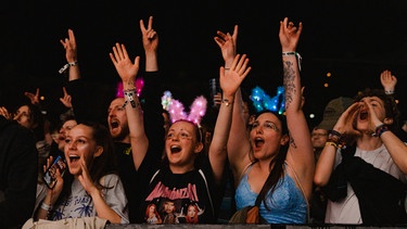 Impression bei Nacht der ersten Publikumsreihe: Die Besucher:innen feiern mit erhobenen Händen auf einem Konzert des PULS Open Airs 2024 | Bild: BR/Sabrina Wanninger