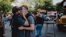 Ein Pärchen küsst sich auf dem Festivalgelände. Im Hintergrund sind Essensstände zu sehen. | Bild: BR/Johanna Schlüter