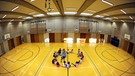 Schüler sitzen in der Turnhalle um den Mittelkreis herum.  | Bild: dpa/ Daniel Reinhardt