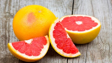 Eine aufgeschnittene Grapefruit mit tiefrotem Fruchtfleisch liegt auf einem Holztisch.  | Bild: mauritius images / YAY Media AS / Alamy / Alamy Stock Photos