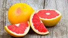 Eine aufgeschnittene Grapefruit mit tiefrotem Fruchtfleisch liegt auf einem Holztisch.  | Bild: mauritius images / YAY Media AS / Alamy / Alamy Stock Photos