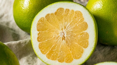 Auf einem hölzernem Untergrund liegt eine aufgeschnittene goldene Pomelo. | Bild: mauritius images / Brent Hofacker / Alamy / Alamy Stock Photos