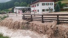 17.07.2021, Bayern, Bischofswiesen: Wasser fließt über einen Platz vor einem Haus. Der Landkreis Berchtesgadener Land hat nach starkem Regen wegen Hochwassers den Katastrophenfall ausgerufen. | Bild: dpa-Bildfunk/Kilian Pfeiffer