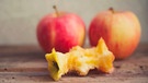 Apfelbutzen liegt auf einem Holztisch, dahinter zwei Äpfel | Bild: mauritius images / Giuseppe Esposito / Alamy / Alamy Stock Photos