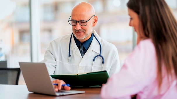 Eine Patientin im Gespräch mit einem Arzt an einem Schreibtisch | Bild: mauritius images / György Barna / Alamy / Alamy Stock Fotos