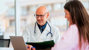 Eine Patientin im Gespräch mit einem Arzt an einem Schreibtisch | Bild: mauritius images / György Barna / Alamy / Alamy Stock Fotos