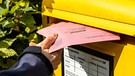 Ein Mann wirft Briefwahl Unterlagen mit Stimmzettel in einen gelben Briefkasten der Deutschen Post | Bild: mauritius images / Chromorange / Michael Bihlmayer