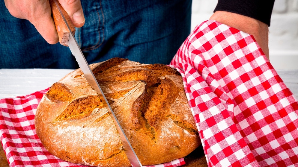 Mann schneidet Brot auf einem Holzbrett. | Bild: mauritius images / Klaus Hoffmann / Alamy / Alamy Stock Photos