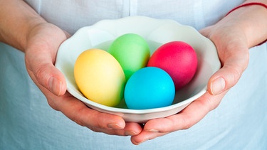 Hände halten eine Schüssel mit bunt gefärbten Eiern in der Hand | Bild: mauritius images / Rafal Stachura / Alamy / Alamy Stock Photos