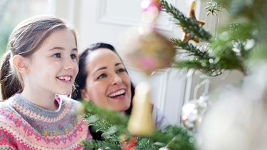 Frau und Mädchen dekorieren Christbaum | Bild: mauritius images / Hoxton / Sam Edwards