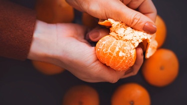 Die Hände einer Frau schälen eine Clementine. | Bild: mauritius images / Valeri Vatel / Alamy / Alamy Stock Fotos