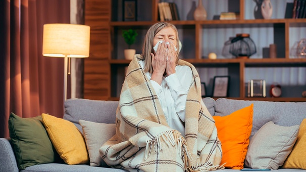 Eine Frau sitzt auf dem Sofa und schneuzt sich | Bild: mauritius images / Liubomyr Vorona / Alamy / Alamy Stock Photos