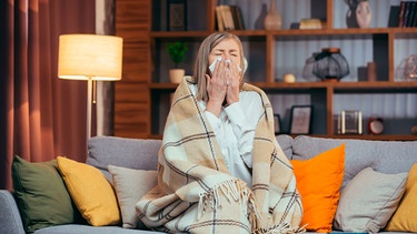 Eine Frau sitzt auf dem Sofa und schneuzt sich | Bild: mauritius images / Liubomyr Vorona / Alamy / Alamy Stock Photos