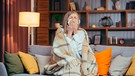 Eine Frau sitzt auf dem Sofa und schneuzt sich | Bild: mauritius images / Liubomyr Vorona / Alamy / Alamy Stock Photos