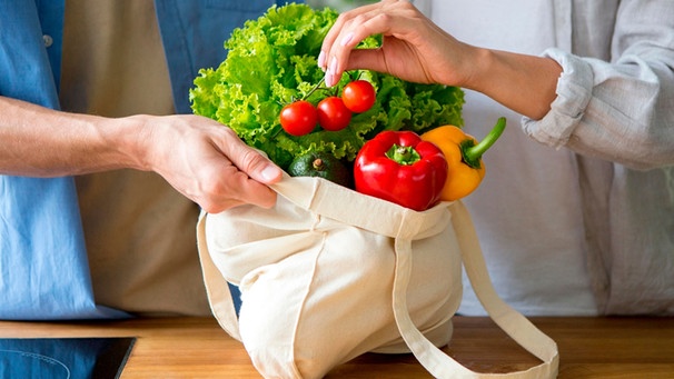 Hand holt aus einer Einkaufstasche mit Gemüse eine Rispe Tomaten heraus | Bild: mauritius images / Prostock-studio / Alamy / Alamy Stock Photos