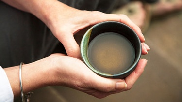 Frau hält eine Tasse mit grünem Tee in den Händen. | Bild: mauritius images