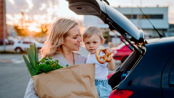 Eine Mutter mit Kleinkind auf dem Arm auf einem Supermarkt-Parkplatz | Bild: mauritius images / Jozef Polc / Alamy / Alamy Stock Photos