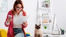 Eine Frau hat ihr Handy und ein Stück Papier in der Hand und freut sich | Bild: mauritius images / LightField Studios Inc. / Alamy / Alamy Stock Photos