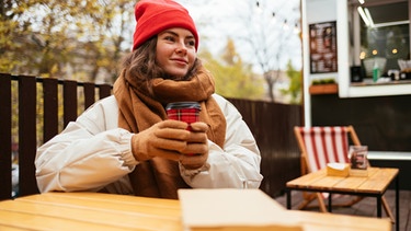 Junge Frau sitzt in einem Outdoor-Cafè | Bild: mauritius images / Westend61 / Alev