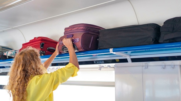 Frau hebt Gepäckstück in die Gepäckablage eines Zugs | Bild: mauritius images / Irina Shatilova / Alamy / Alamy Stock Photos