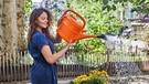 Eine Frau gießt ihren Garten mit einer orangen Gießkanne | Bild: mauritius images / Westend61 / Jo Kirchherr