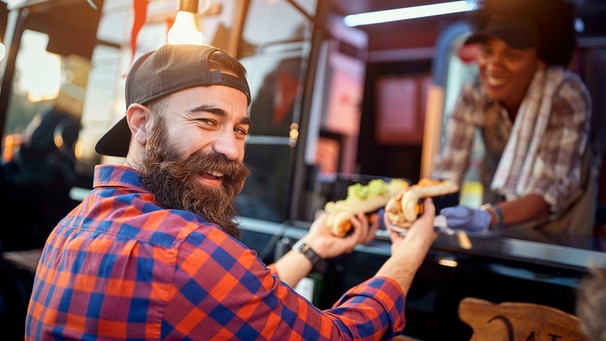 Gut gelaunter Mann holt Essen von einem Food-Truck. | Bild: mauritius images / Igor Mojzes / Alamy / Alamy Stock Fotos