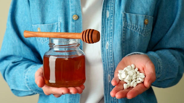 Ein Mann hält in der einen Hand ein Glas Honig, in der anderen zahlreiche Tabletten. | Bild: mauritius images / Atlas Studio / Alamy / Alamy Stock Fotos