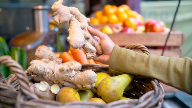 Die Hand einer Frau hält an einem Marktstand ein großes Stück Ingwerwurzelknolle in der Hand | Bild: mauritius images / Westend61 / Anthony Photography